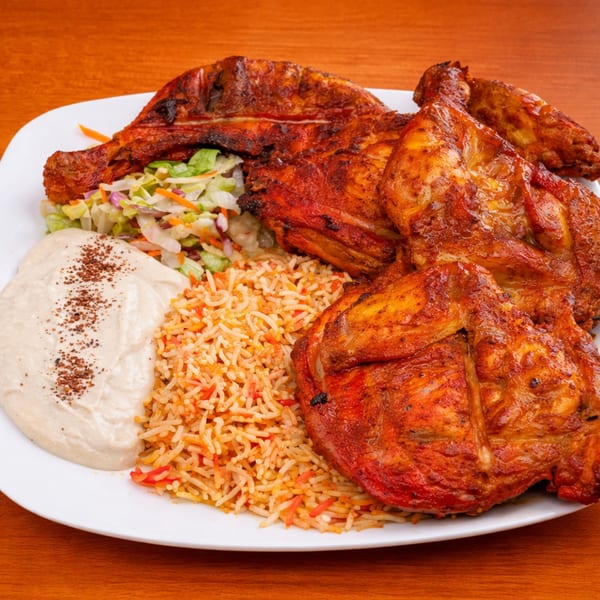 Halal Bites' grilled chicken with rice, salad, and a creamy sauce on a white plate.
