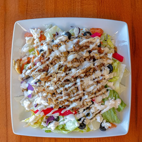Halal Bites' chicken shawarma salad with lettuce, olives, and white sauce on a white plate.